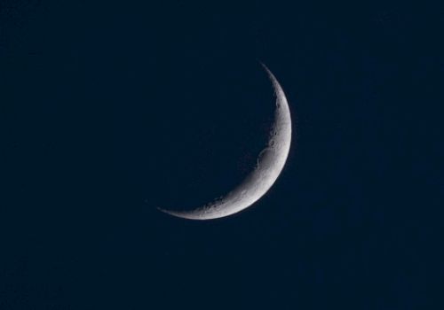 A crescent moon is positioned against a dark night sky, with its thin illuminated edge creating a serene and beautiful celestial image.