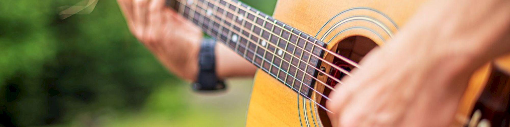 A person is playing an acoustic guitar outdoors, with sunlight shining on the guitar.