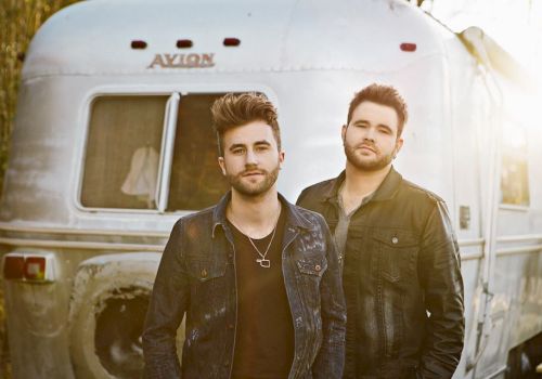 Two men stand in front of a silver trailer labeled 