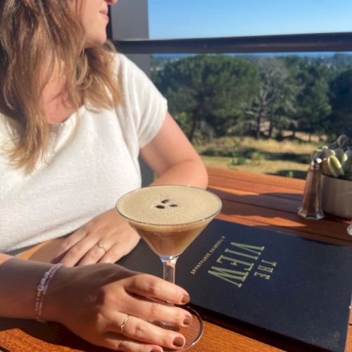 A person is sitting at a table with a cocktail and a menu labeled 