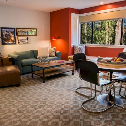 A cozy living room with a sofa, chairs, coffee table, dining table, and large window with a view of trees.