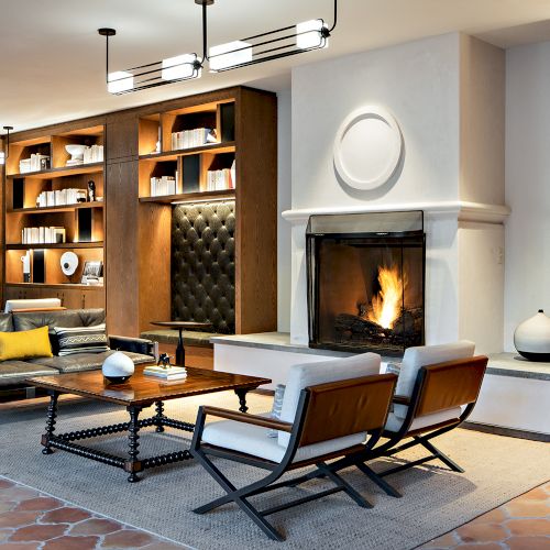 A stylish living room with a fireplace, bookshelves, modern furniture, and decorative objects on a rug and tables, creating a cozy atmosphere.