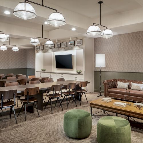 A modern conference room with rows of chairs, a large screen, decorative lights, a leather couch, and a coffee table with green stools.