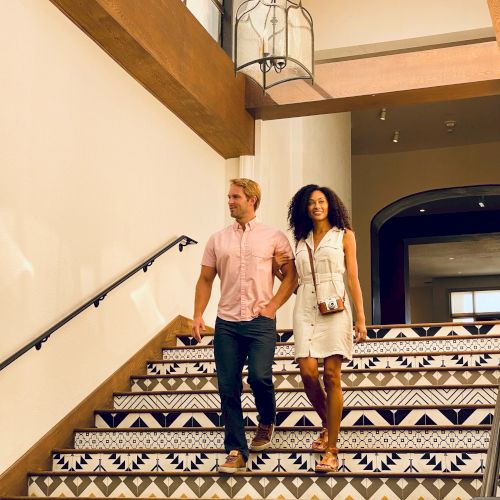 A couple is walking down a stylish staircase adorned with patterned tiles in a well-lit, modern setting.