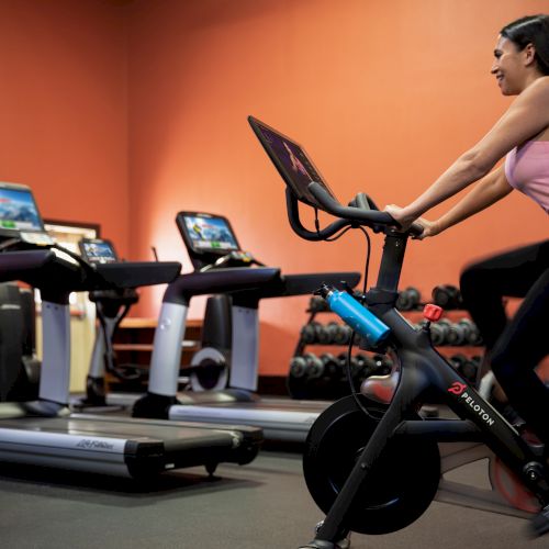 A person is riding a stationary bike in a gym with treadmills and other gym equipment in the background.