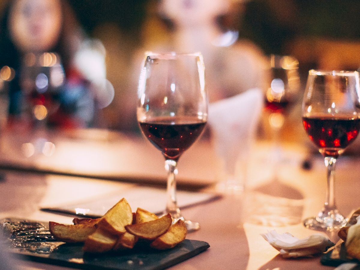 The image shows a table set with glasses of red wine and plates of food, including sliced items, suggesting a social gathering or wine tasting event.