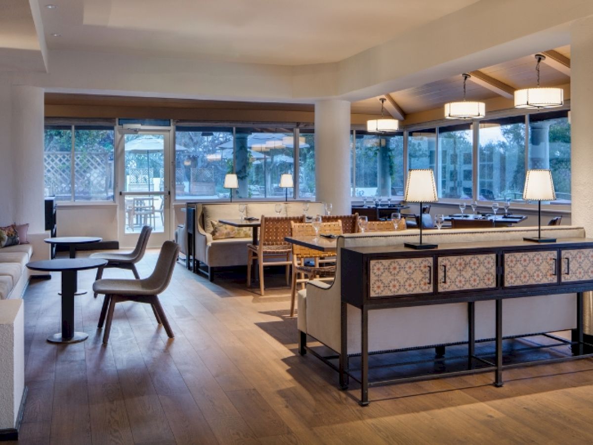 The image shows an elegant, well-lit dining area with tables, chairs, and modern decor. The room features large windows and stylish lighting fixtures.